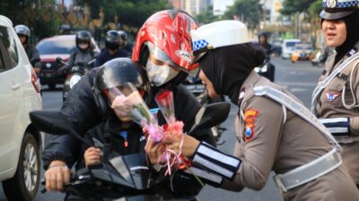 BAGIKAN: Anggota Polwan Polresta Malang Kota saat membagikan bunga dan coklat kepada masyarakat pengendara
