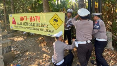 SPANDUK,: Anggota Kamsel Satlantas Polres Batu saat memasang spanduk rawan kecelakaan dan bencana